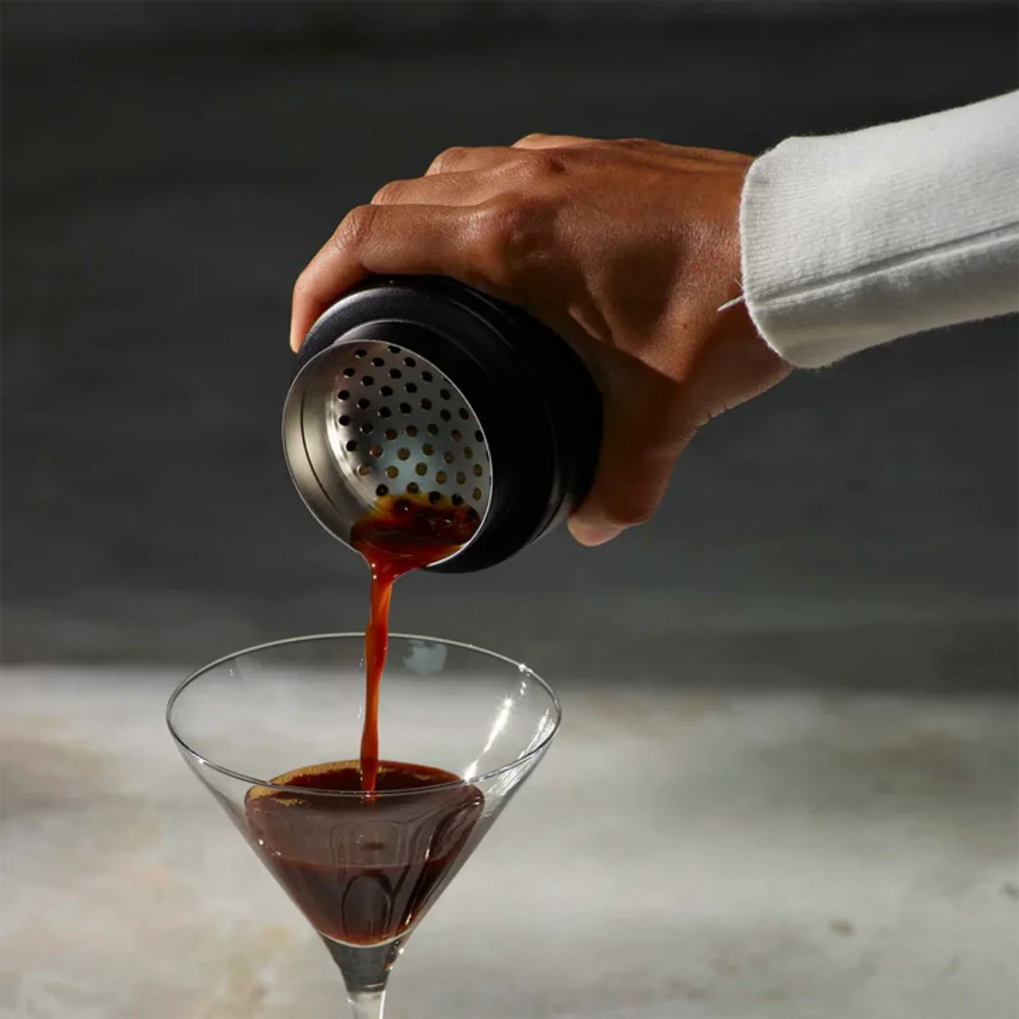 Hand pouring a coffee from a Breville The Shake & Take Black Truffle - BEA050BTR0ZNA1 into a martini glass on a neutral background