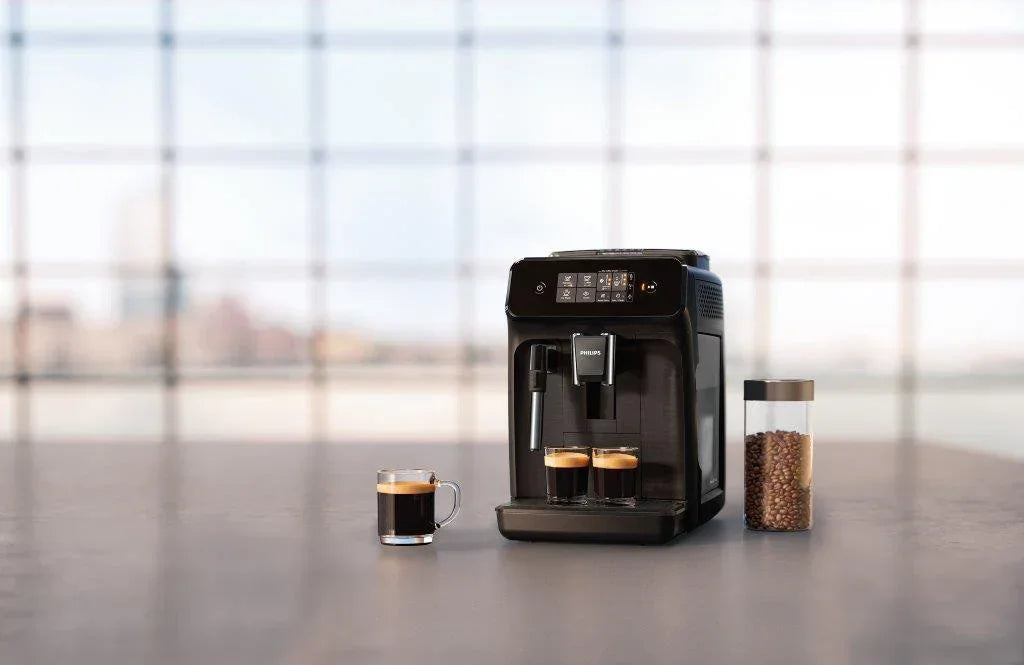 Black espresso machine on a table with a cup of coffee and a jar of coffee beans, blurred window background.