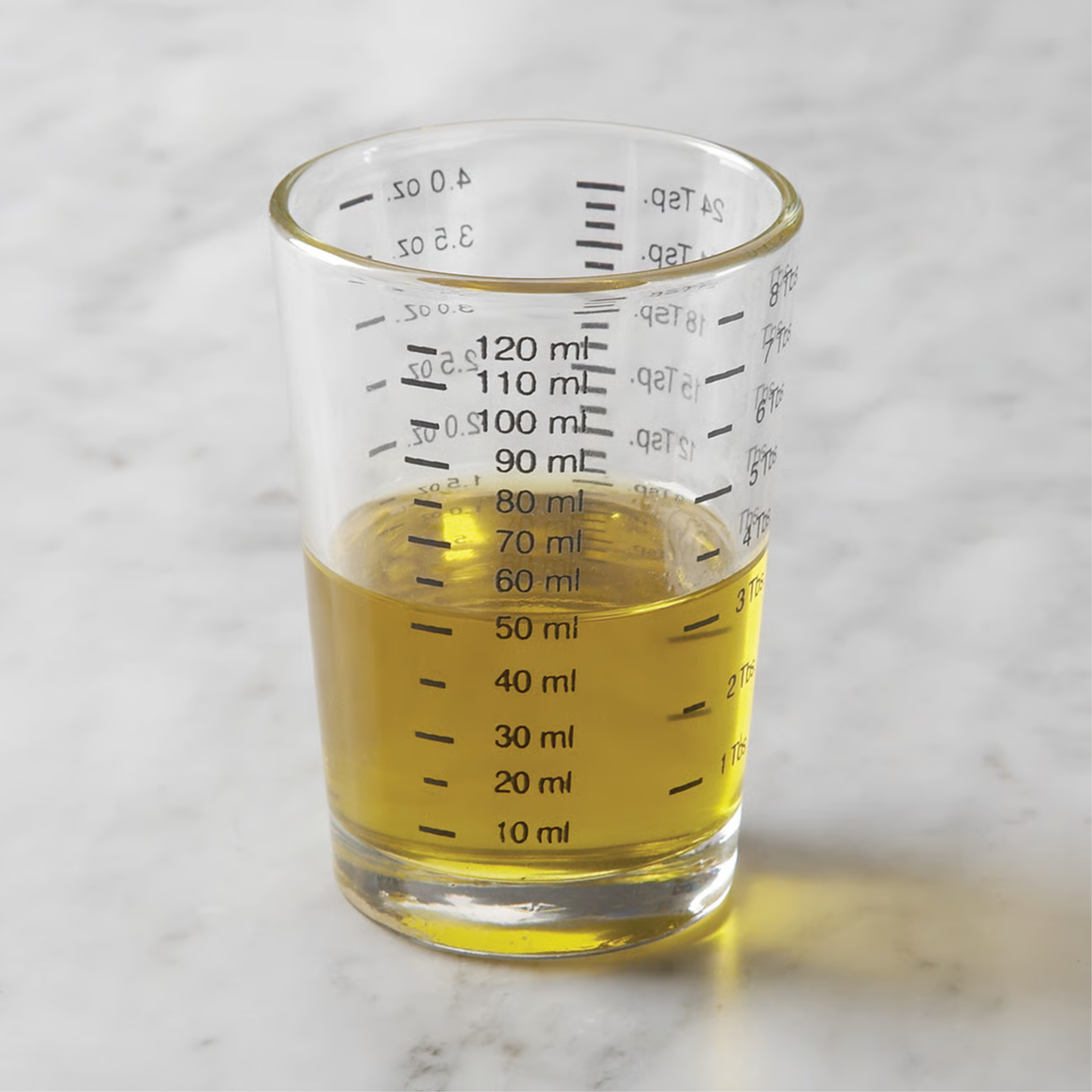 Shot glass holding yellow liquid against a marble background.