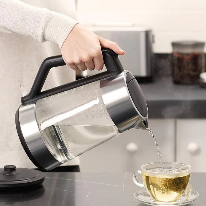 Person pouring water from a glass kettle into a cup on a kitchen counter.