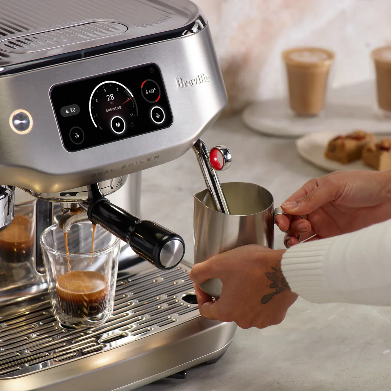 Breville espresso machine being used to make coffee, with a person holding a metal cup.