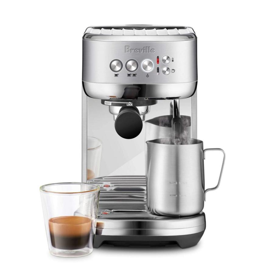 Stainless steel espresso machine with Breville branding, frothing pitcher, and espresso in a glass cup at the front.