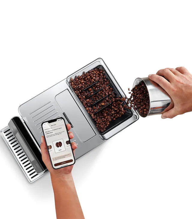 Coffee grinder with coffee beans being added and a smartphone app displayed on a white background