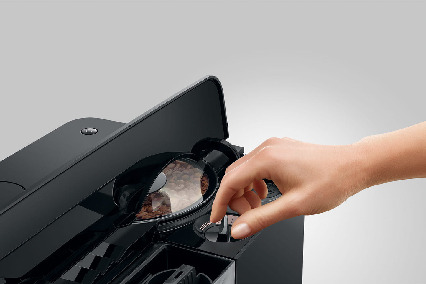 Person using a black espresso machine with a clear lid on a gray background