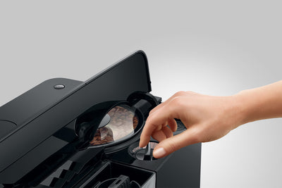 Person using a black espresso machine with a clear lid on a gray background