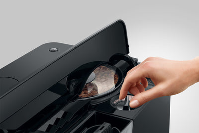 Hand placing a coffee pod into a black coffee machine on a light gray background
