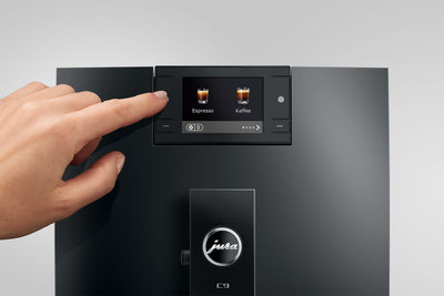 Hand pressing a button on a modern coffee machine with a Jura logo.