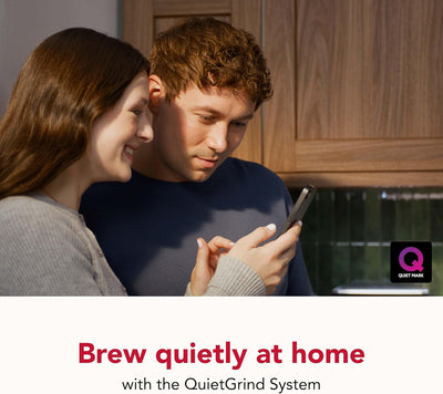 Two people looking at a phone with a QuietGrind System advertisement in the background.