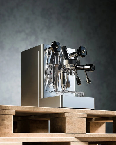 Silver espresso machine on a wooden platform with a gray background