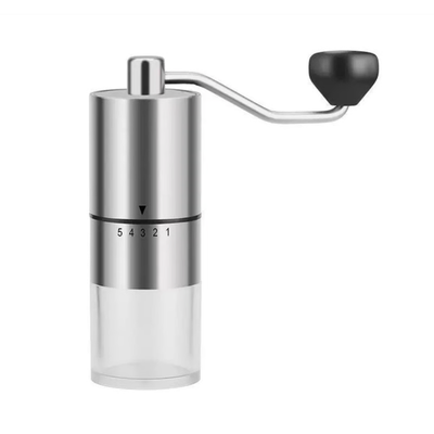 A manual coffee grinder with a brushed stainless steel body, a clear lower chamber, a curved metal handle, and a black hand wheel, shown on a plain white background.