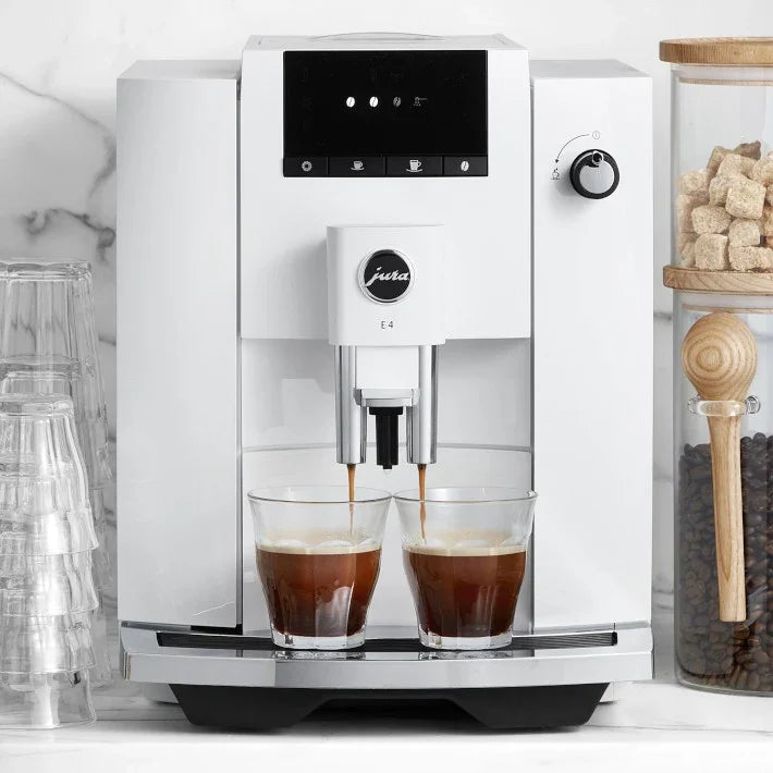 White coffee machine with two glasses of coffee being filled, set against a kitchen backdrop.