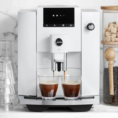 White coffee machine with two glasses of coffee being filled, set against a kitchen backdrop.