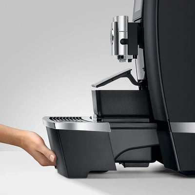 Espresso machine with a hand reaching to open the front panel on a light gray background