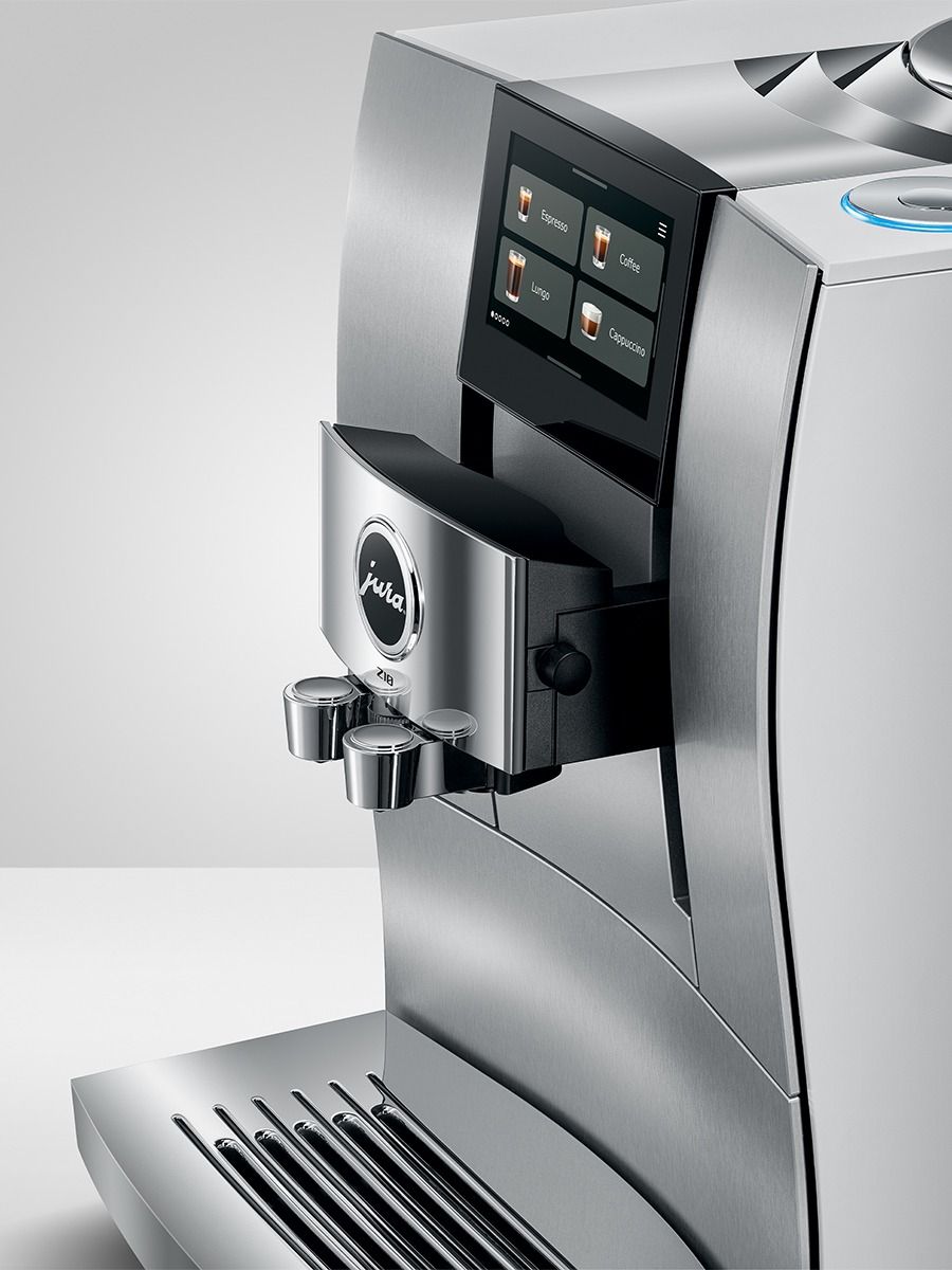 A close-up studio shot of a modern Jura coffee machine in brushed stainless steel with a black control screen and metal drip tray, shown against a light gray background.