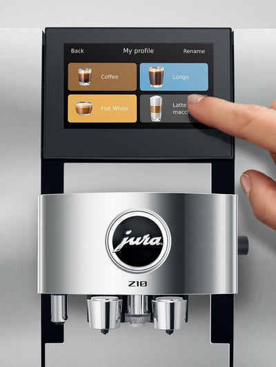 A close-up of a Jura Z10 coffee machine with a human finger touching the touchscreen interface, set against a brushed stainless steel background.