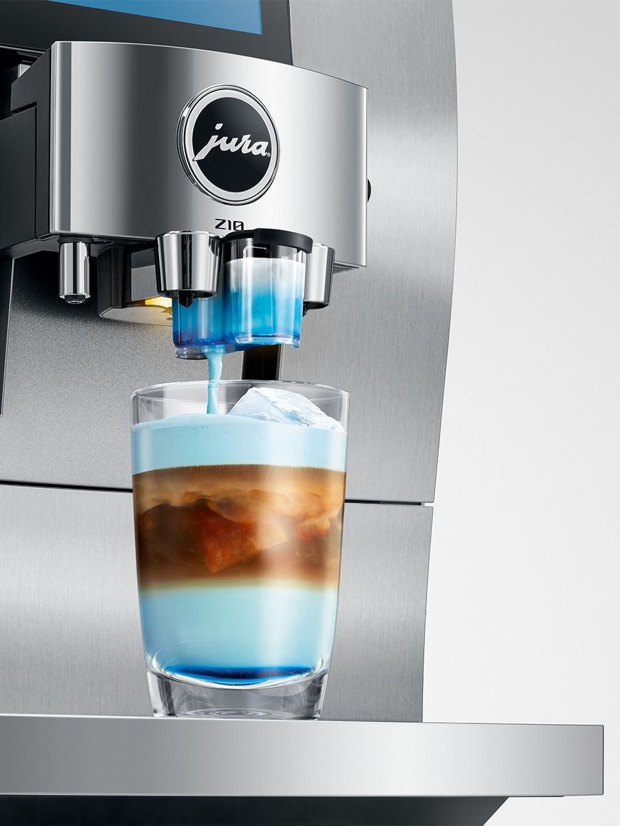 A Jura Z10 espresso machine dispensing layered coffee with blue milk into a clear glass on a stainless steel countertop.