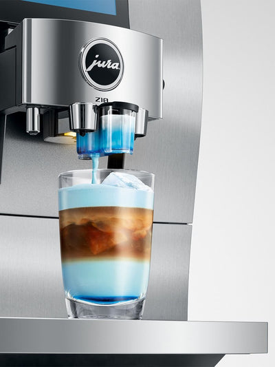 A Jura Z10 espresso machine dispensing layered coffee with blue milk into a clear glass on a stainless steel countertop.